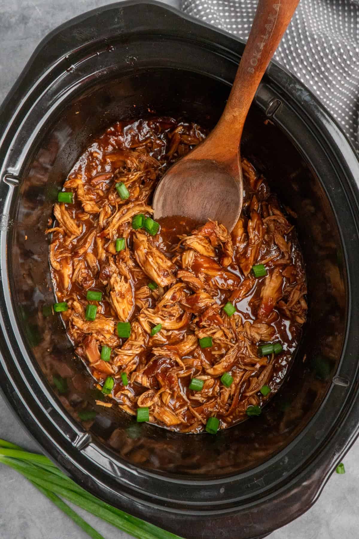 Raspberry chicken in the slow cooker with a wooden spoon scooping up some.