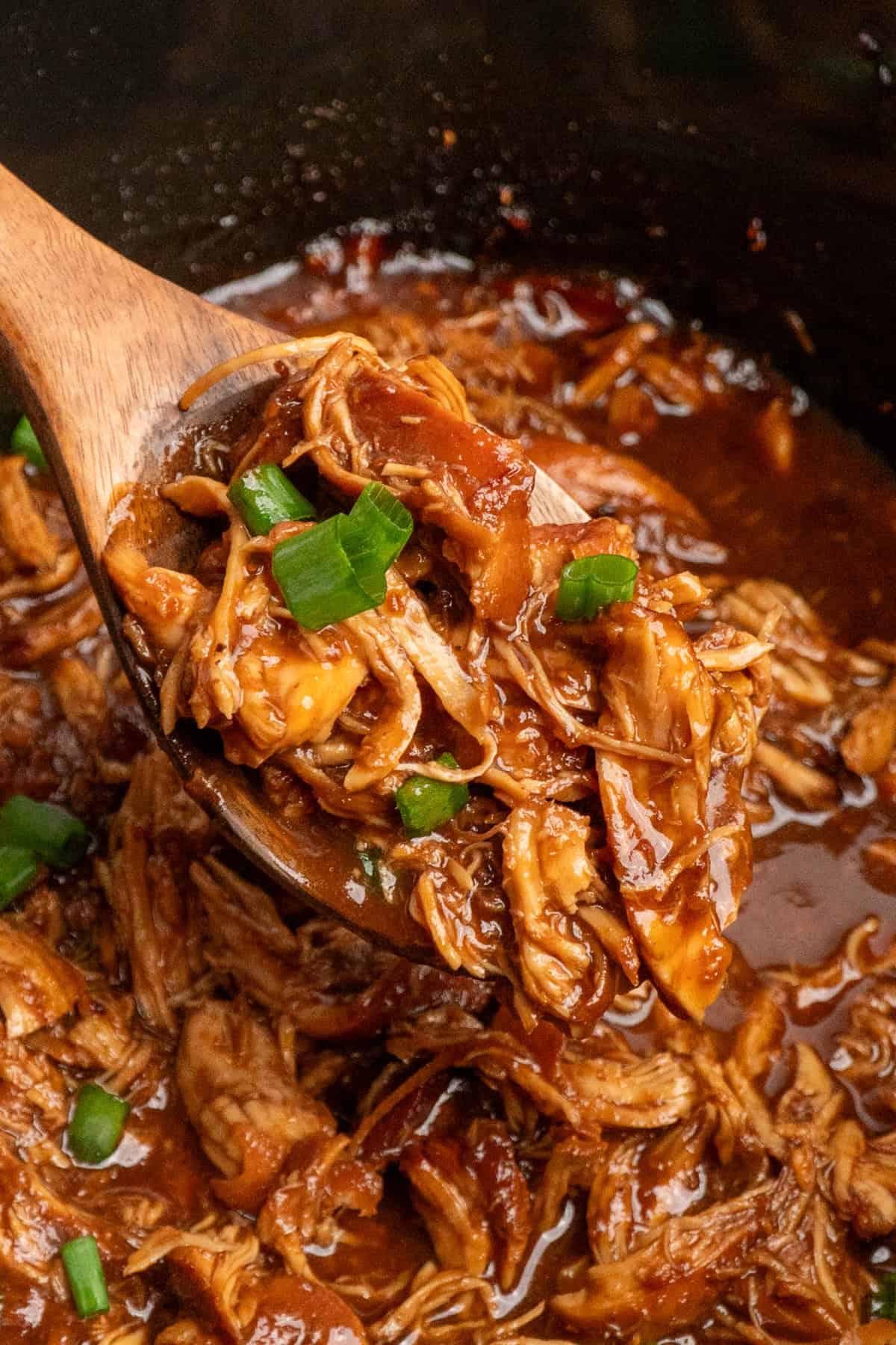 A wooden spoon lifting a serving of raspberry chicken up from the slow cooker.