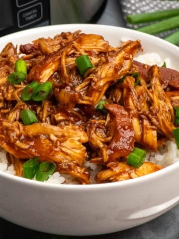 Slow cooker raspberry chicken served up in a bowl on the table over some rice.