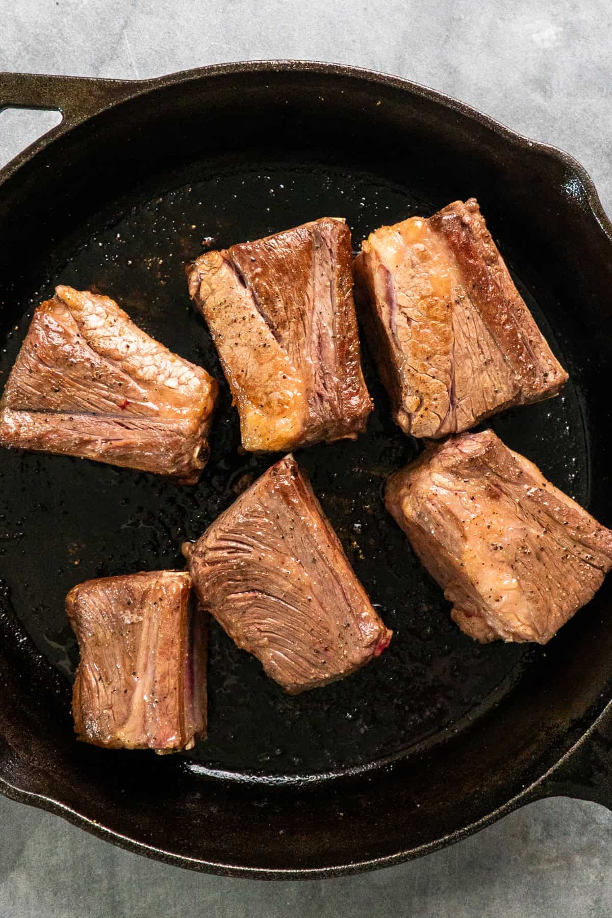 Short ribs being seared in a cast iron skillet.