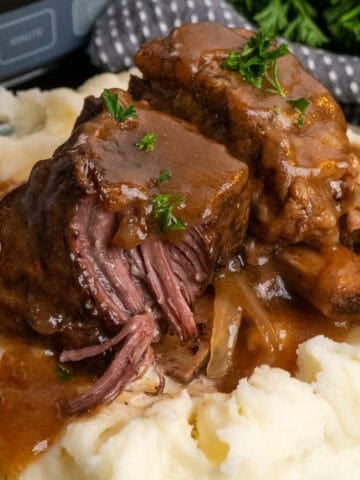 Two short ribs over mashed potatoes and covered in gravy.