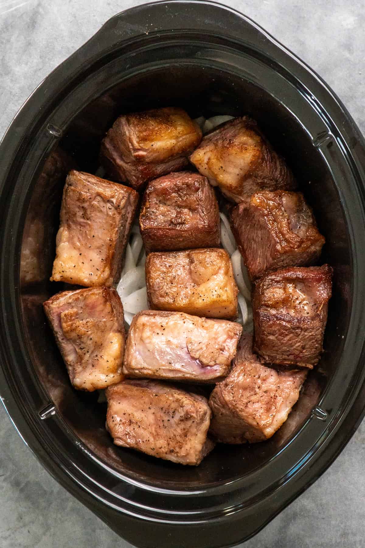 Short ribs on top of onions in a slow cooker.