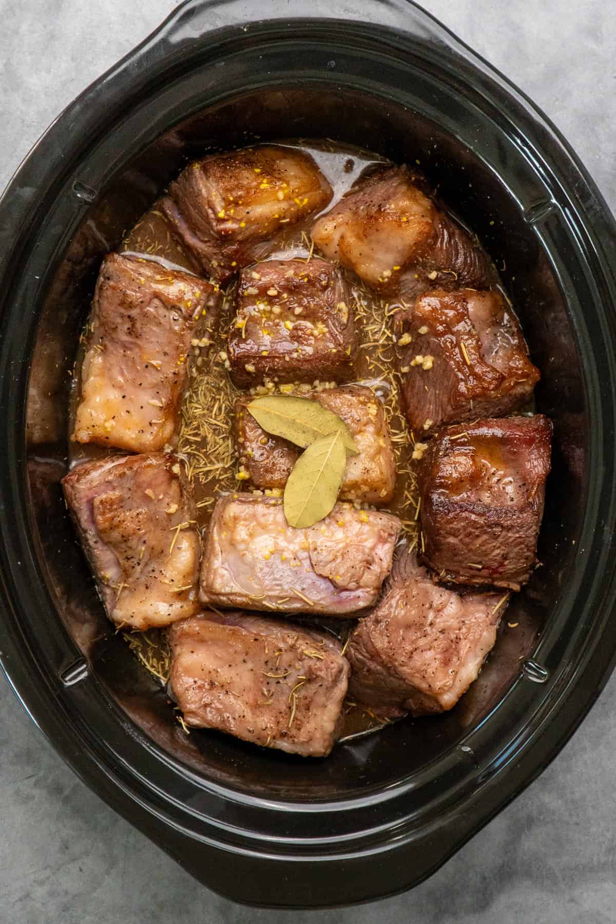 Gravy and short ribs in a slow cooker ready to be cooked.