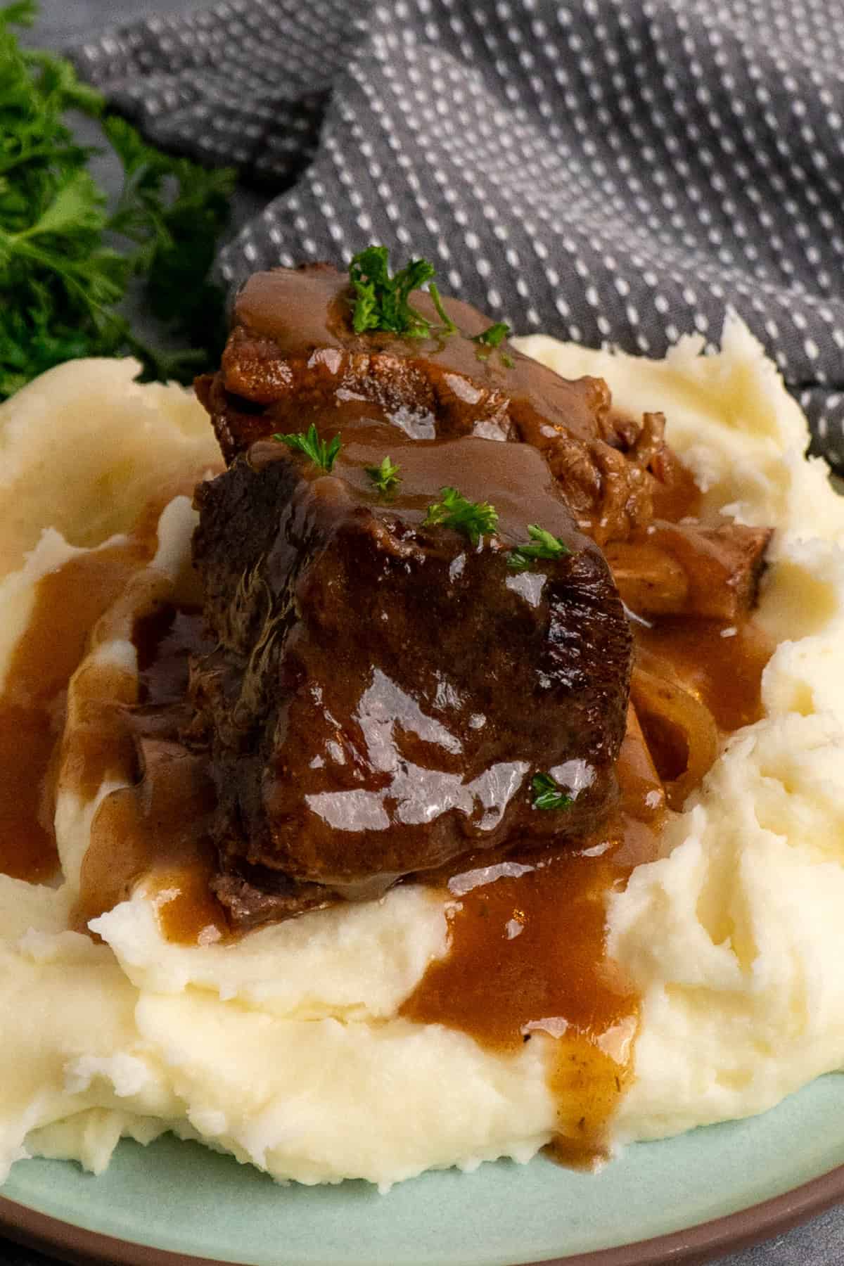 Two short ribs on a plate of mashed potatoes and covered with gravy.