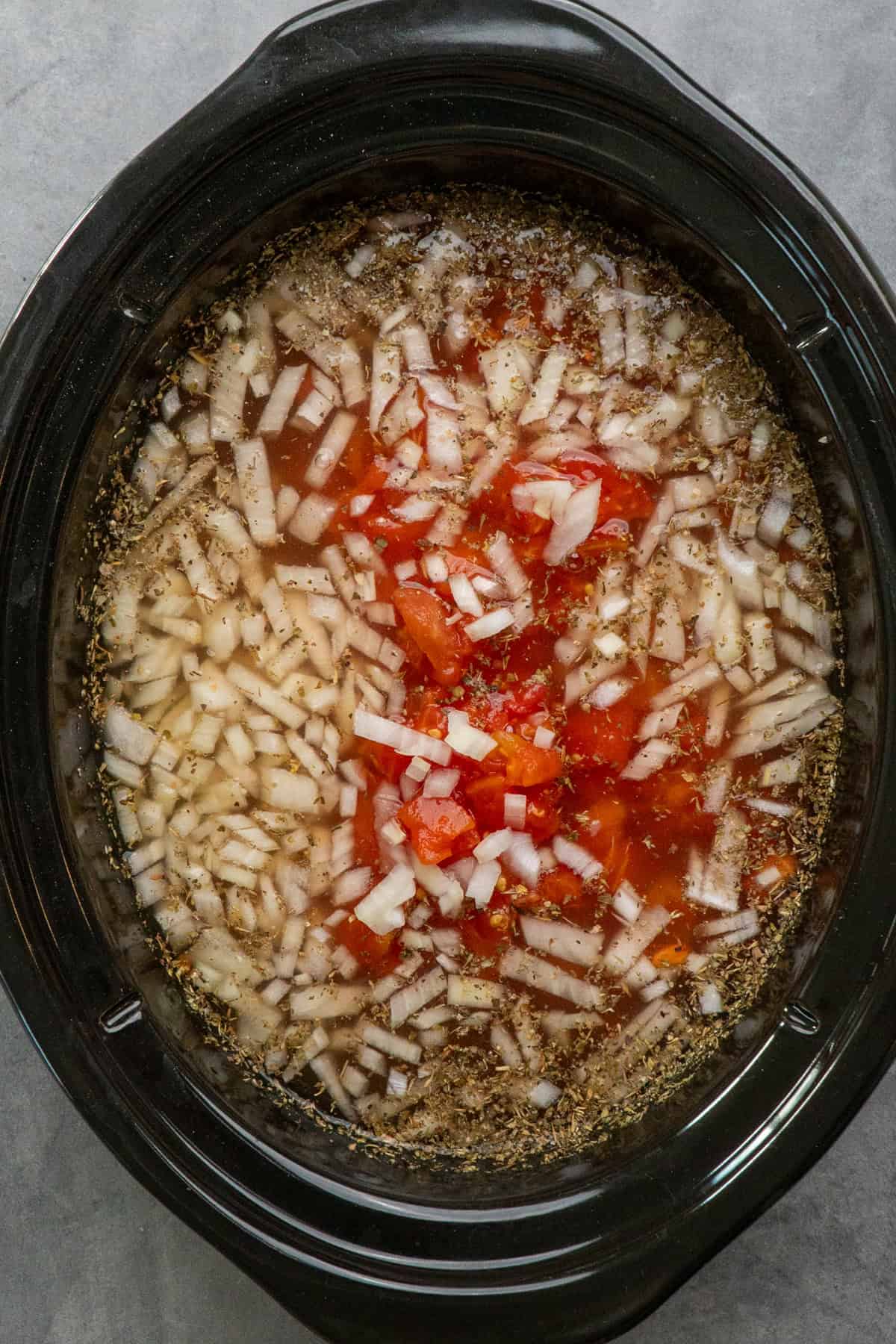 Chicken breast, broth, onions, tomatoes, and seasonings in a crock pot ready to be cooked.