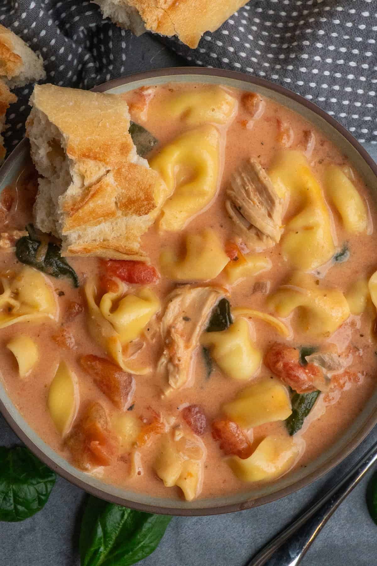 Crock pot chicken tortellini soup in a bowl with a piece of bread in it.