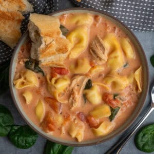 Crock pot chicken tortellini soup in a bowl with a piece of bread in it.