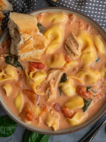 Crock pot chicken tortellini soup in a bowl with a piece of bread in it.