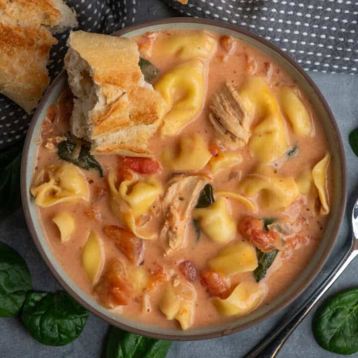 Crock pot chicken tortellini soup in a bowl with a piece of bread in it.