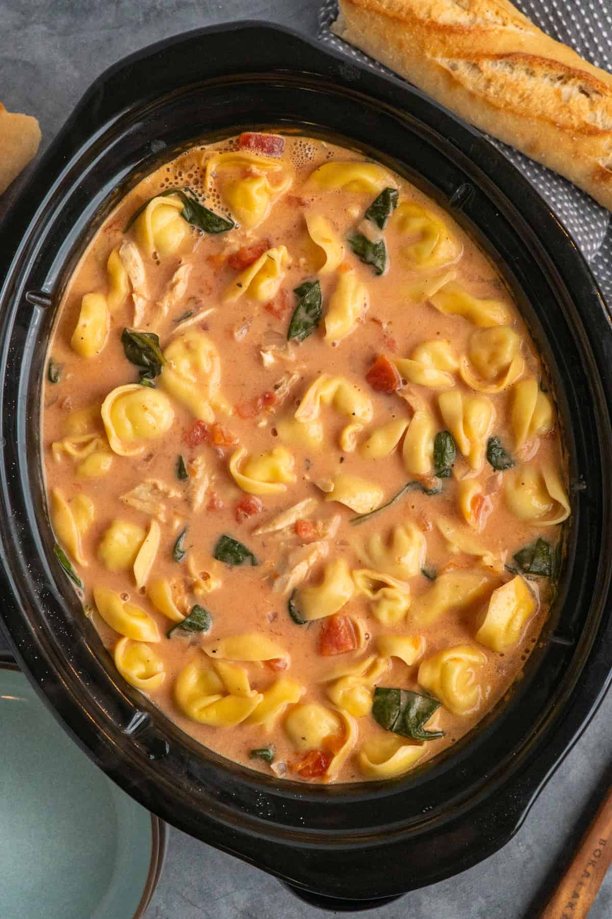 Cooked chicken tortellini soup in a crock pot.