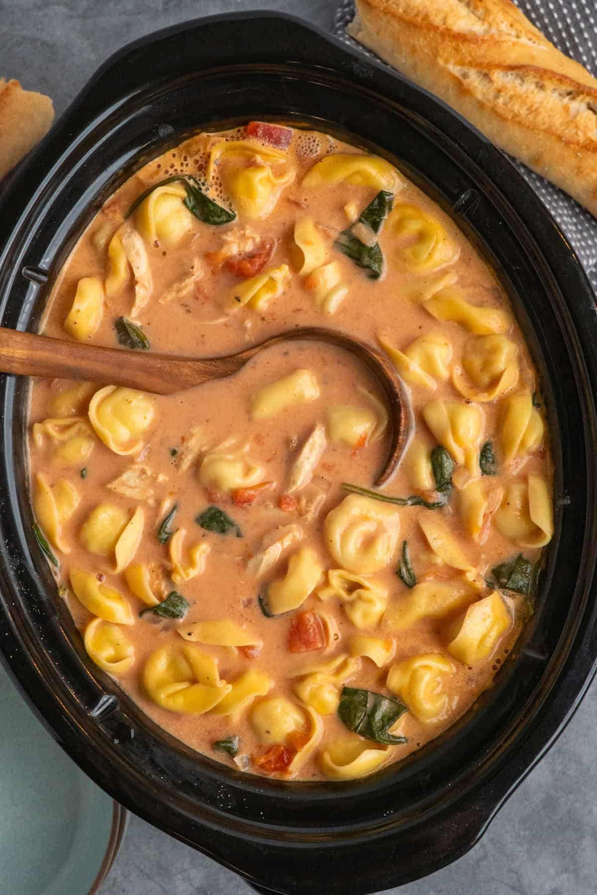 A wooden ladle in a slow cooker full of chicken tortellini soup.