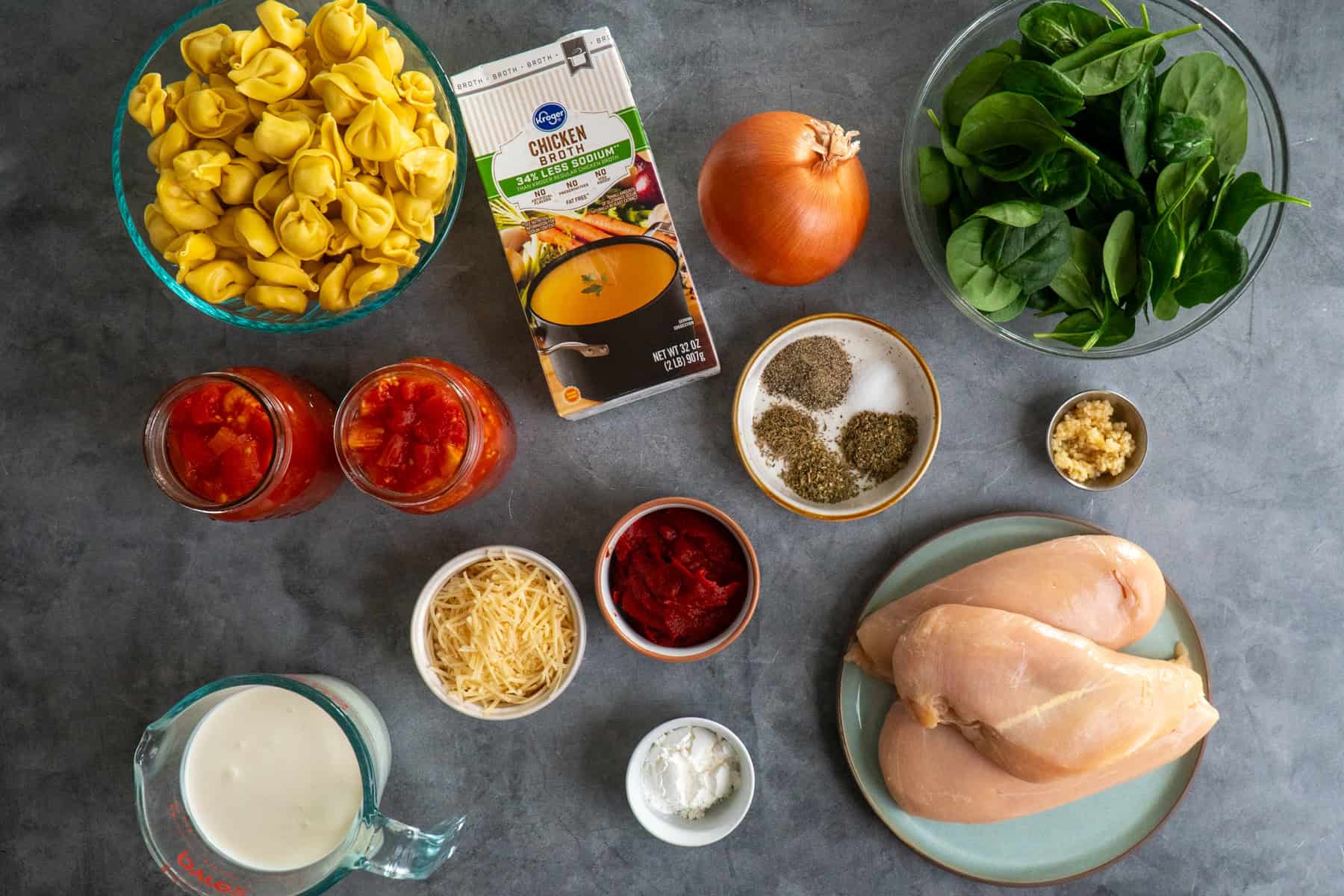 All the ingredients to make chicken tortellini soup on a stone countertop.