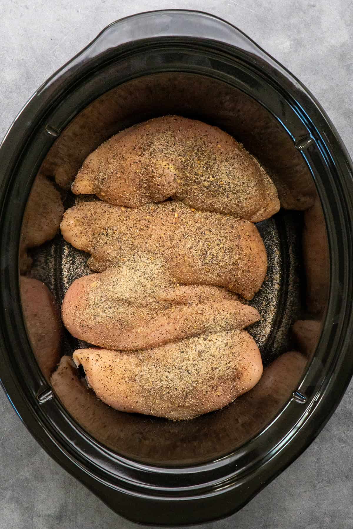 Chicken breasts in a crock pot with seasoning.