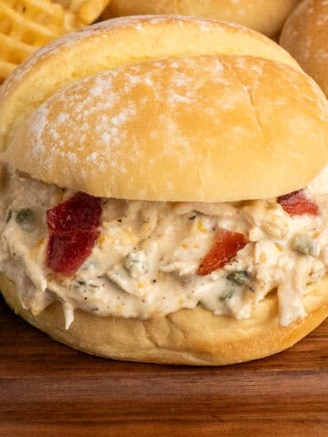 A crock pot jalapeno popper chicken sandwich on a wood cutting board.