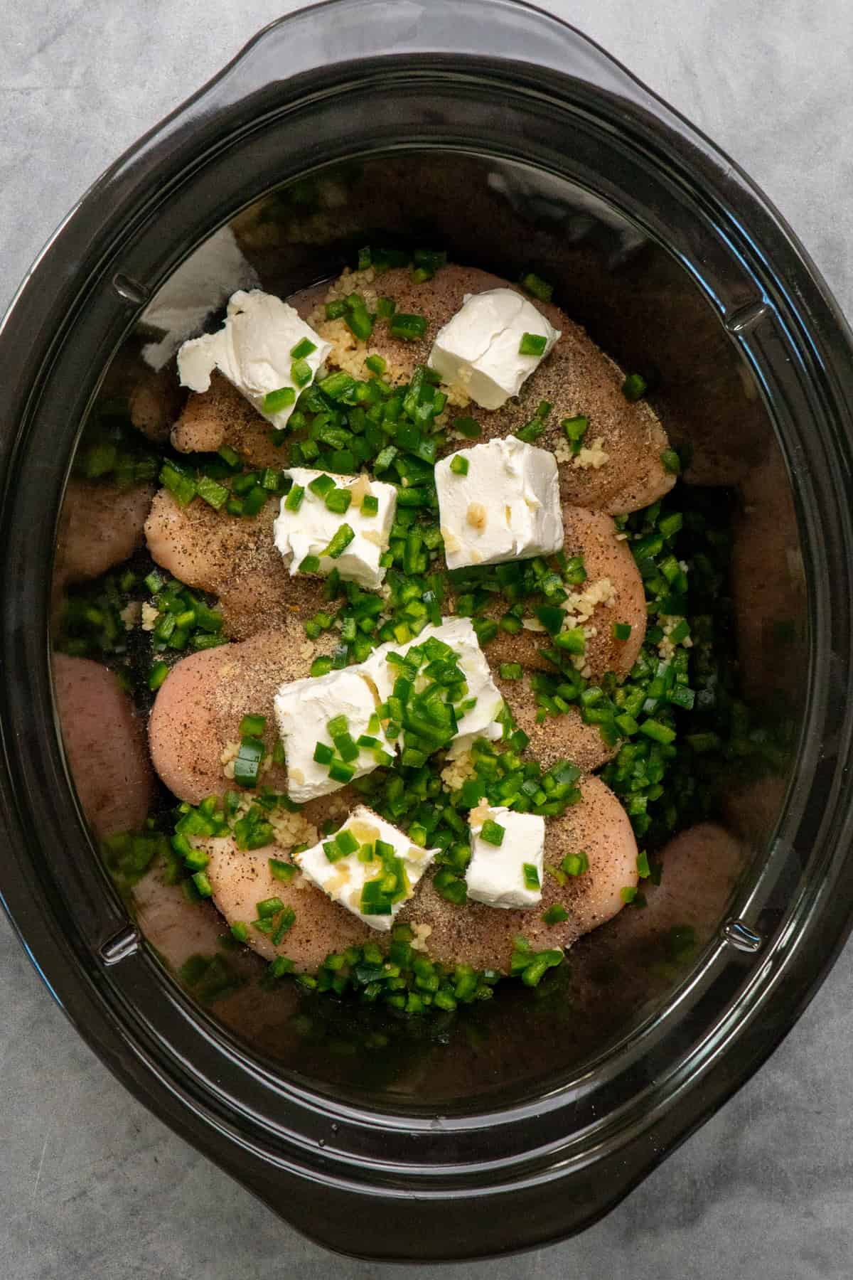 Chicken breasts in a crock pot with garlic, jalapeno and cream cheese on top.