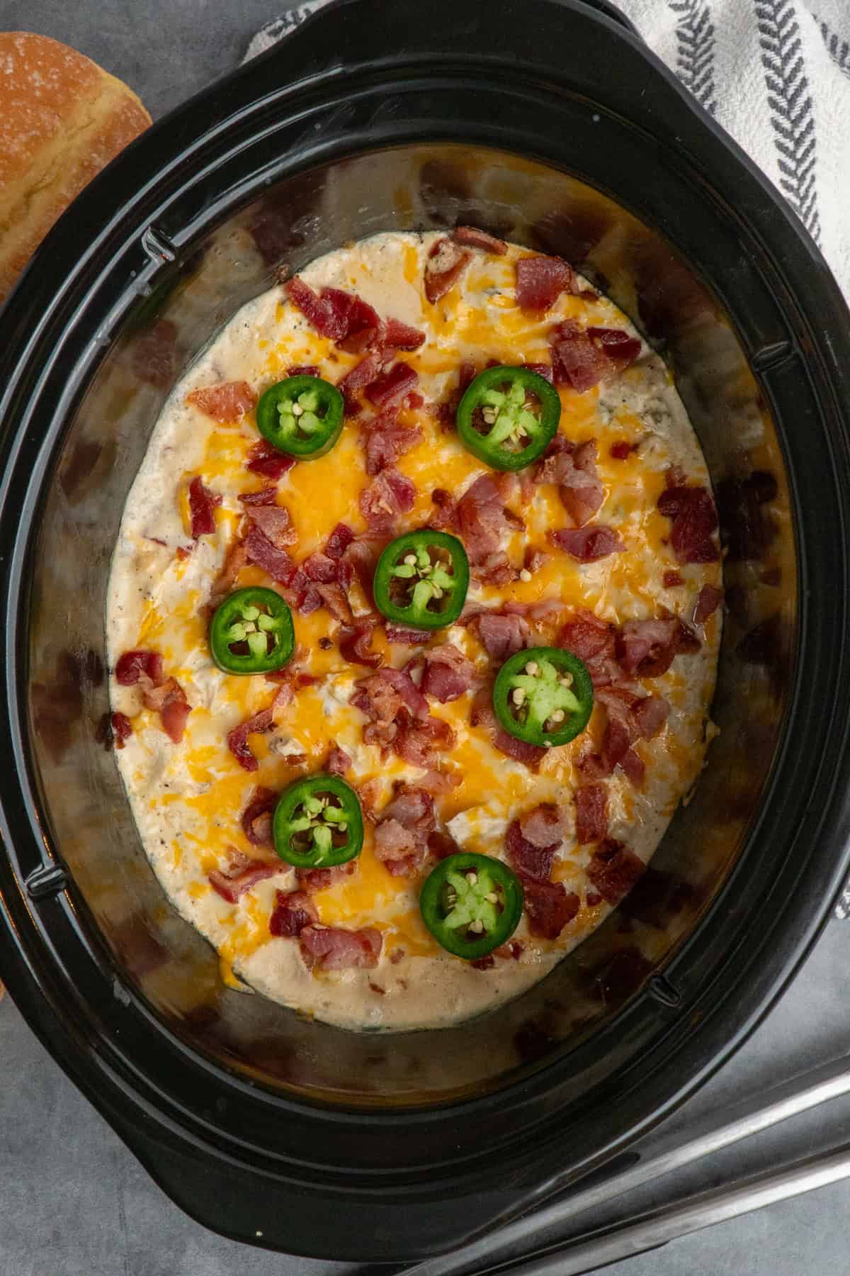 Crock pot jalapeno chicken with melted cheese, bacon and jalapenos on top ready to be served.