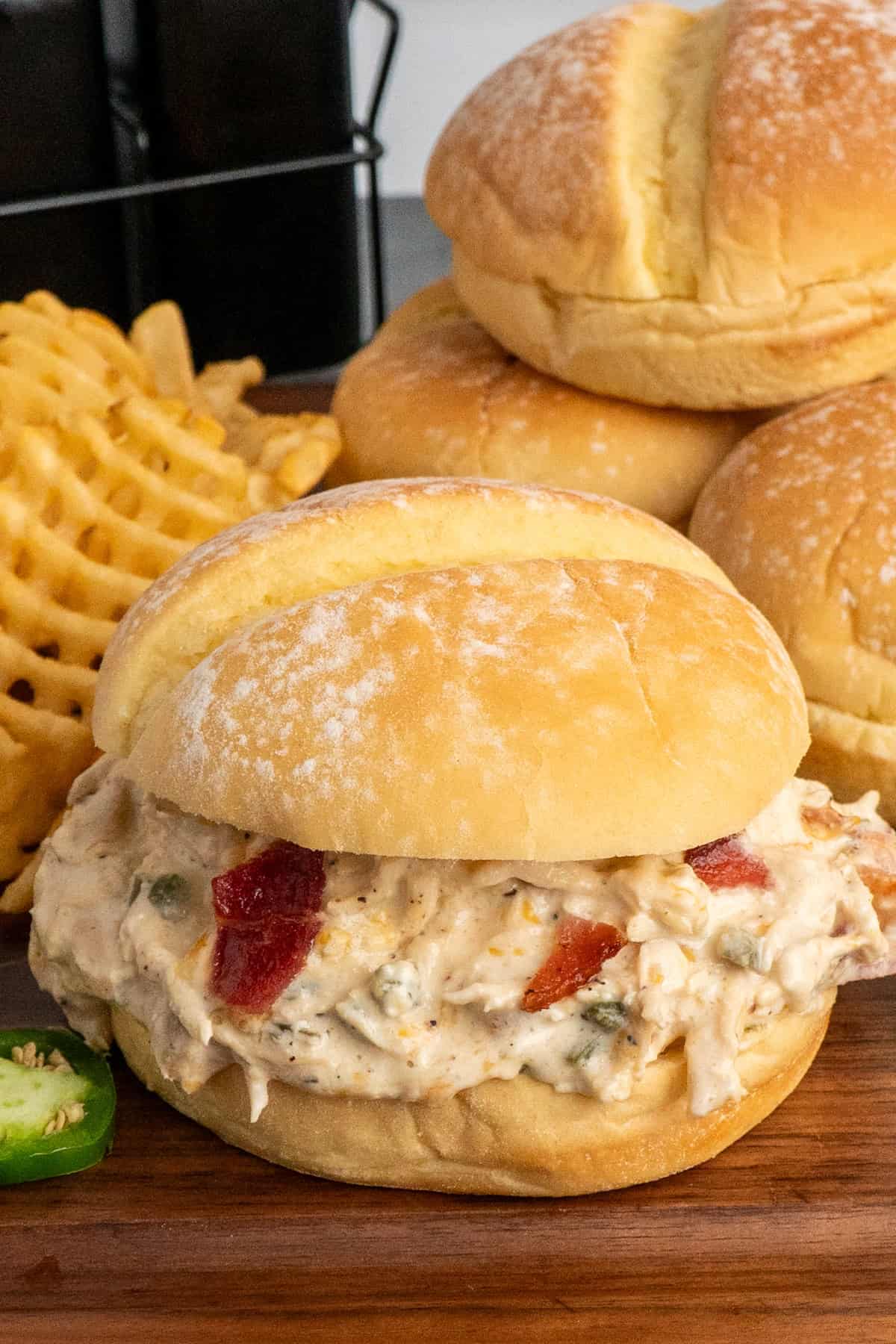 A crock pot jalapeno popper chicken sandwich on a wood cutting board.