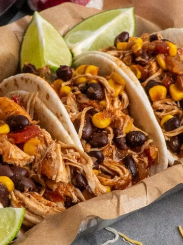 Four crock pot southwest chicken tacos in a tray lined in parchment paper.