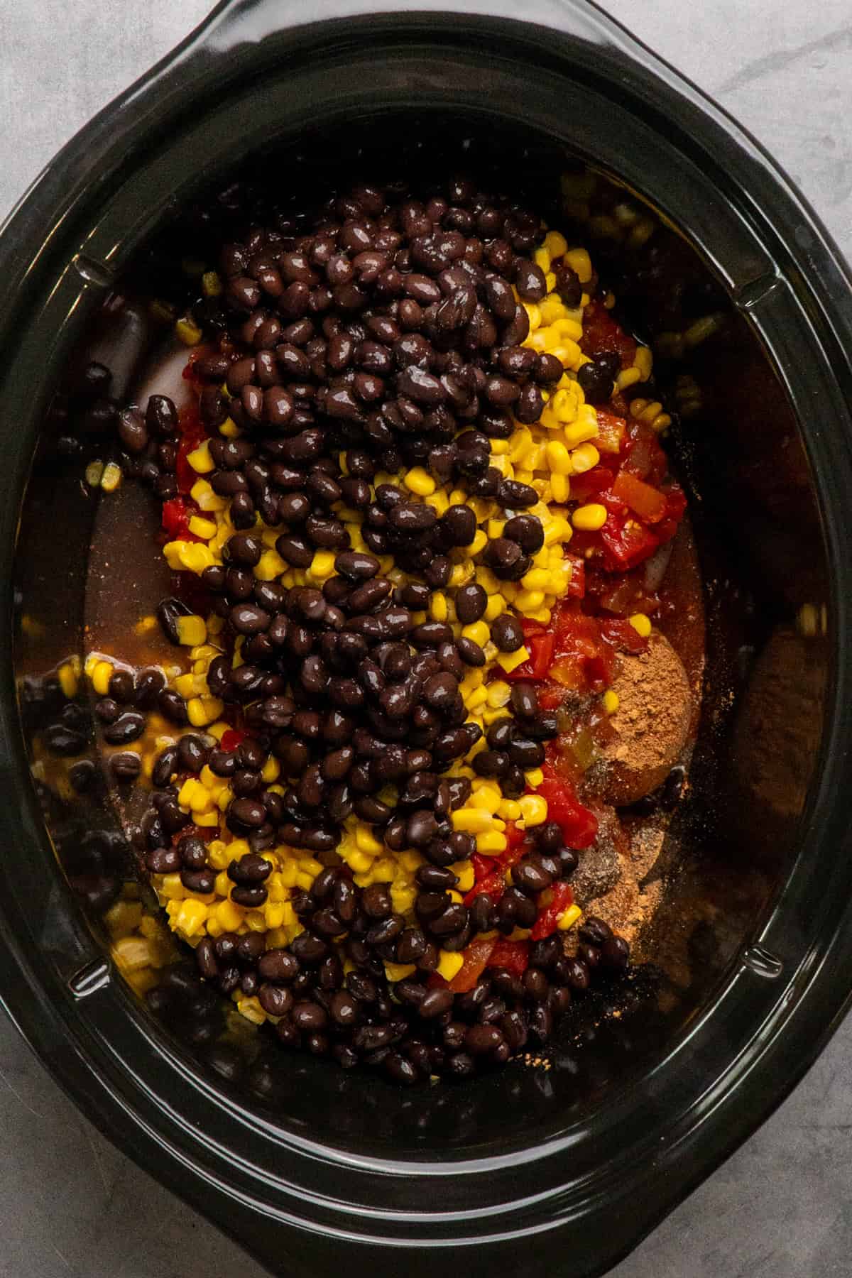 Beans, corn, seasonings, and salsa on top of chicken in a crock pot.