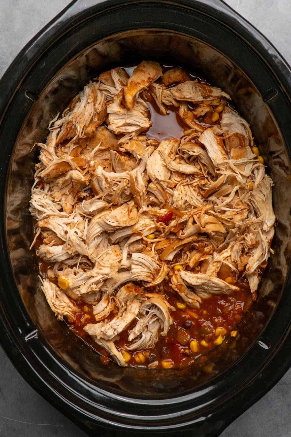 Cooked shredded chicken in a southwest sauce in a slow cooker.