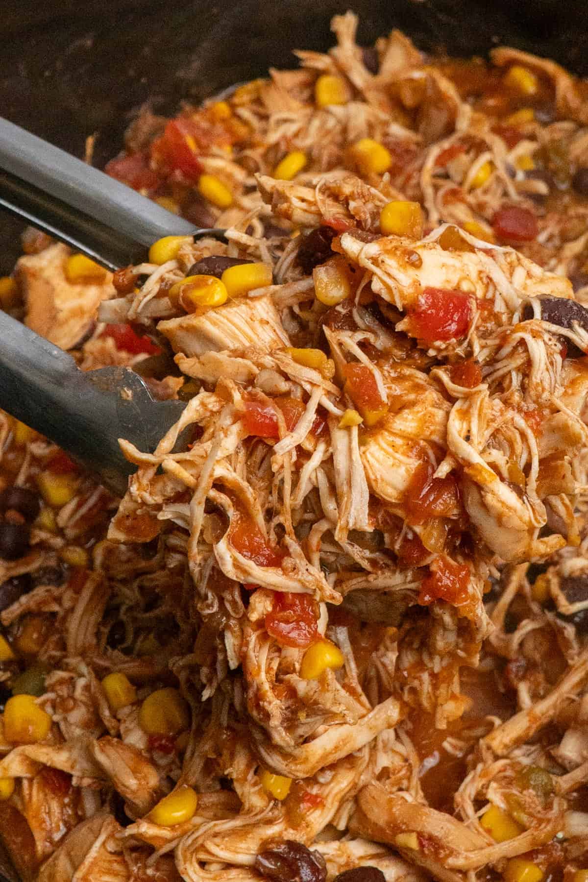 Tongs holding shredded southwest chicken.