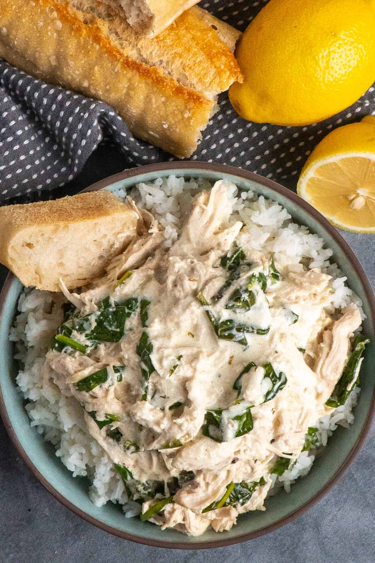 Creamy lemon herb chicken over a bowl of rice with a slice of bread.