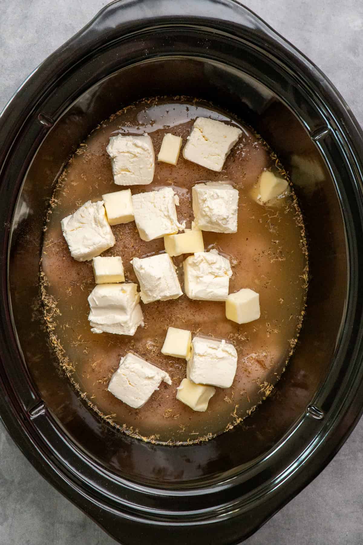 Cream cheese and butter on top of chicken in a slow cooker.