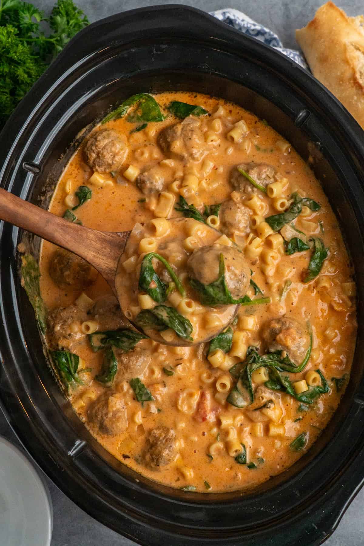 A wooden ladle holding a serving of slow cooker meatball soup.