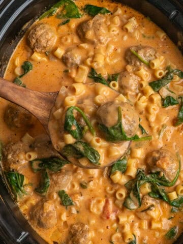 A wooden ladle holding a serving of slow cooker meatball soup.