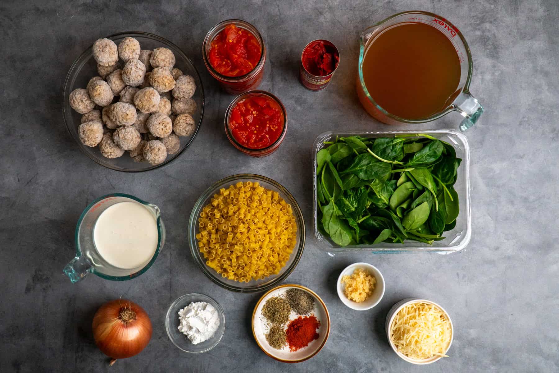 Ingredients to make meatball soup in bowls on a gray countrertop.