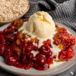 Crock pot cherry cobbler on a plate and topped with vanilla ice cream.