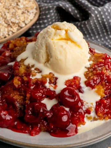 Crock pot cherry cobbler on a plate and topped with vanilla ice cream.