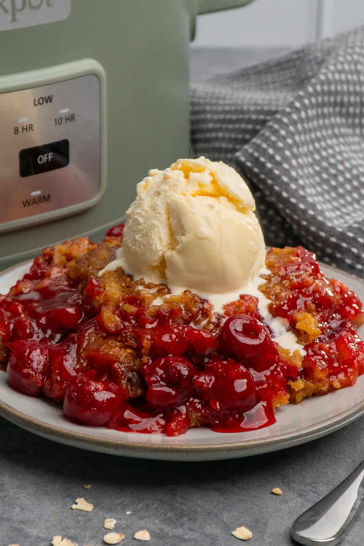 Cherry cobbler on a plate with ice cream on top.