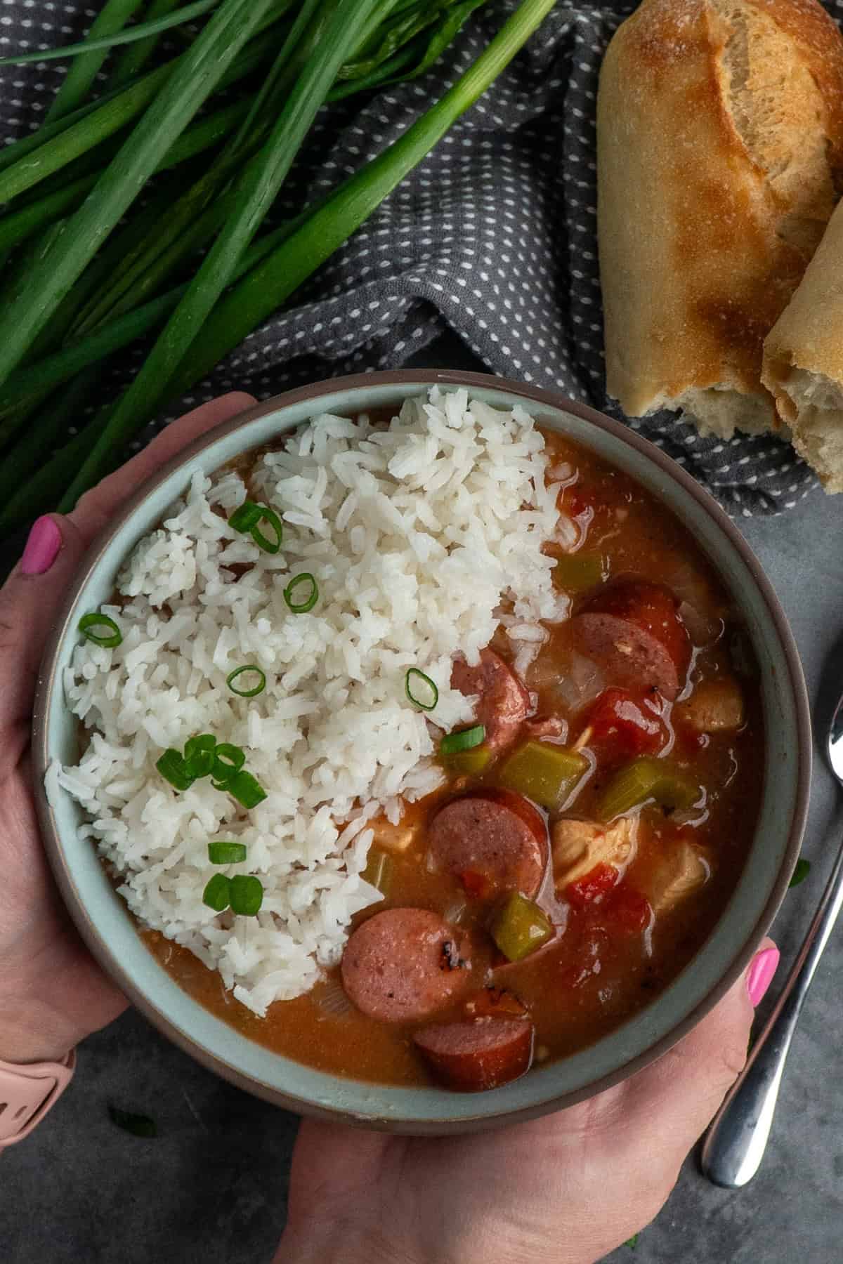 Hands holding a bowl of chicken and sausage gumbo with rice.