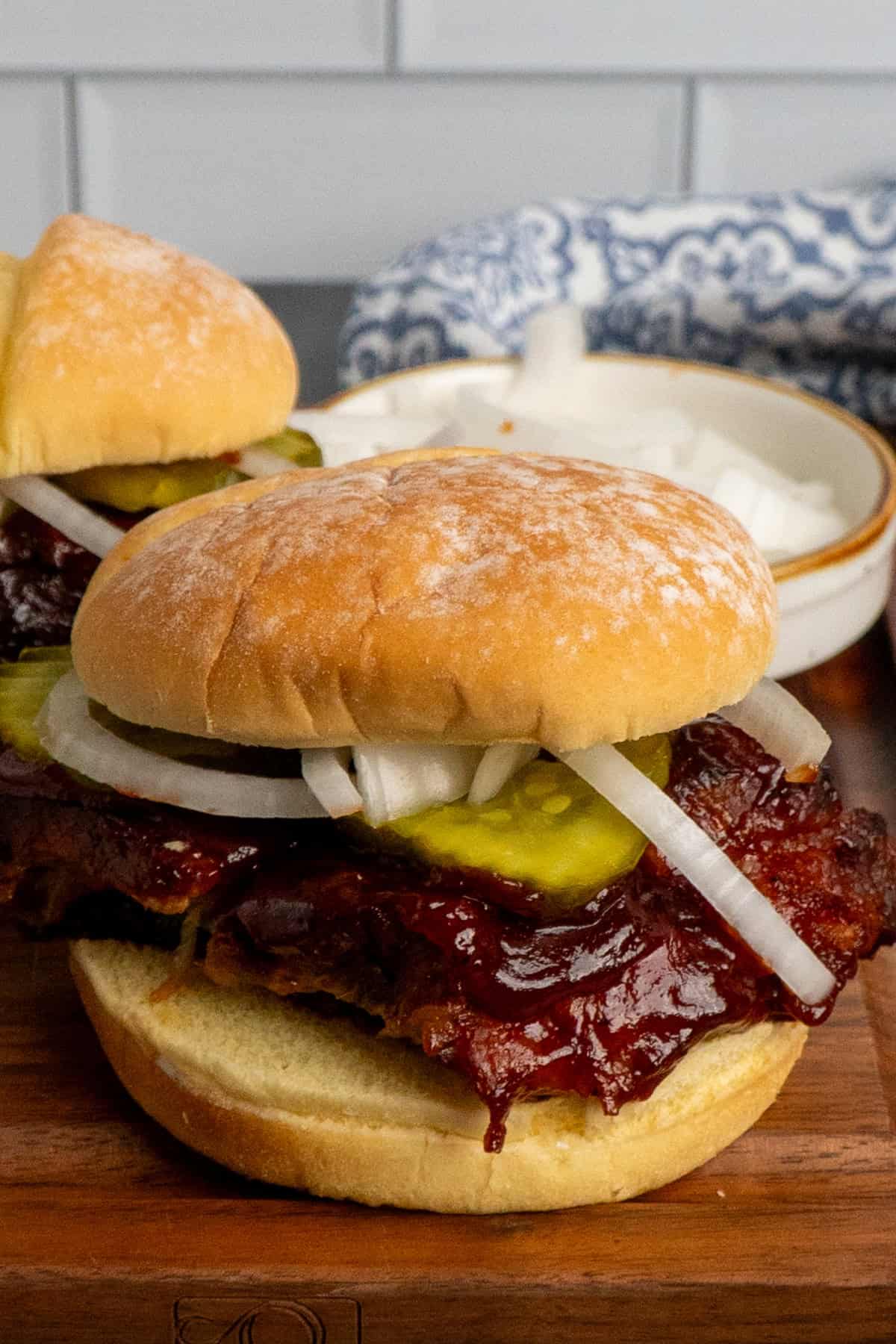 A BBQ pork rib sandwich on a bun with pickles and onions. 