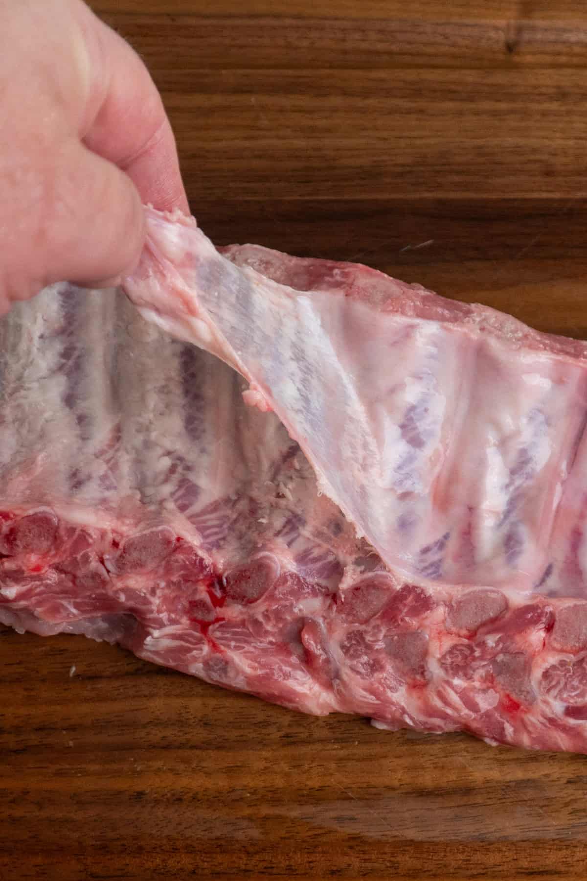 A hand removing the membrane from a rack of baby back ribs.