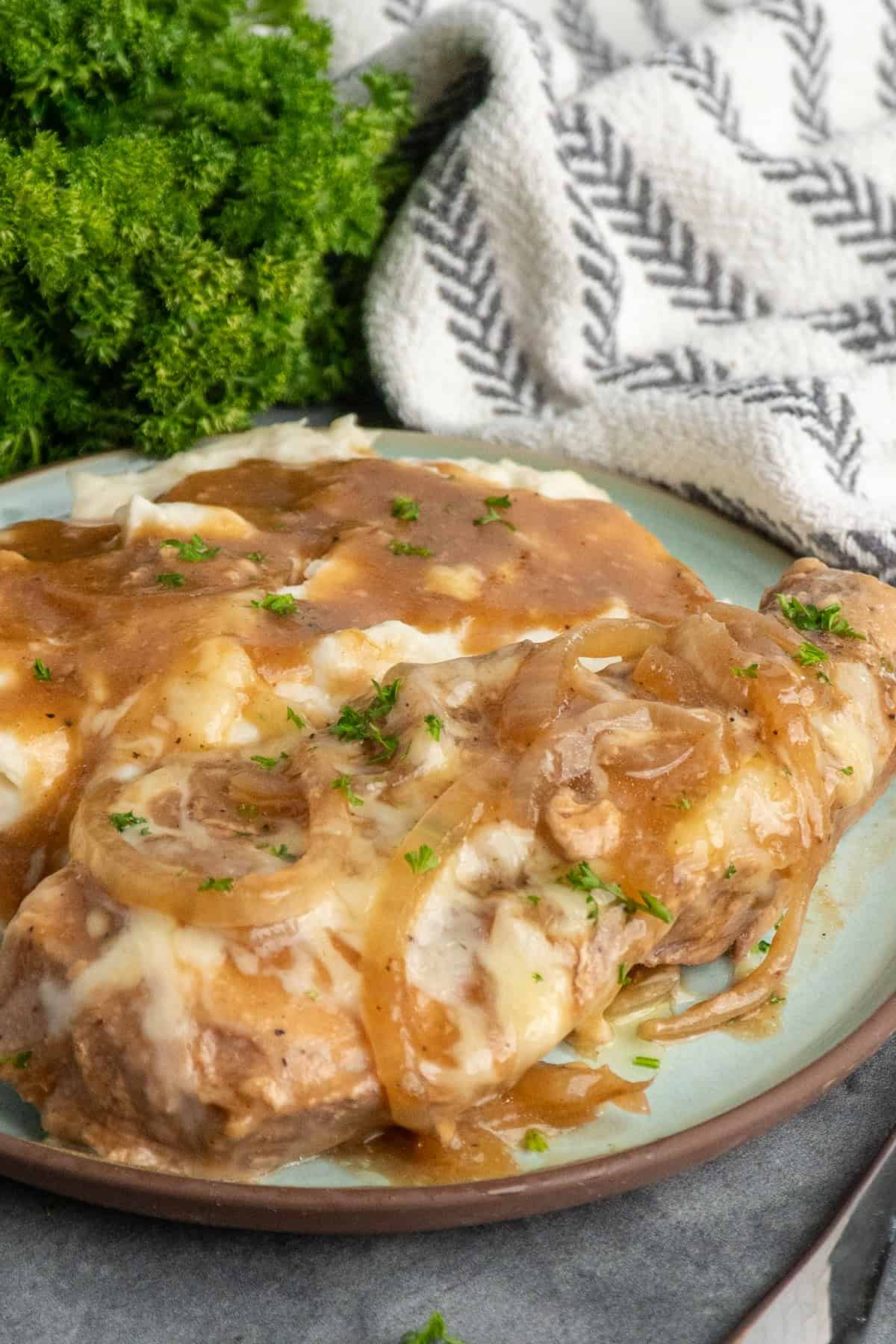 Crock pot French onion pork chops on a plate with mashed potatoes.