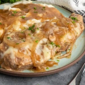 Crock pot French onion pork chops on a plate with mashed potatoes.