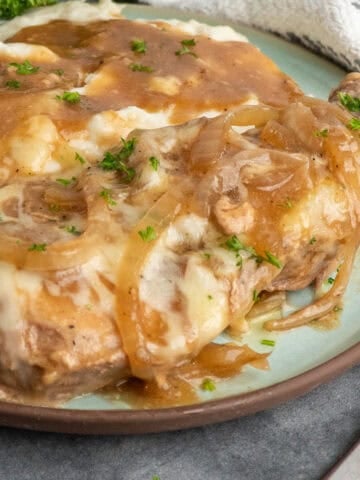 Crock pot French onion pork chops on a plate with mashed potatoes.