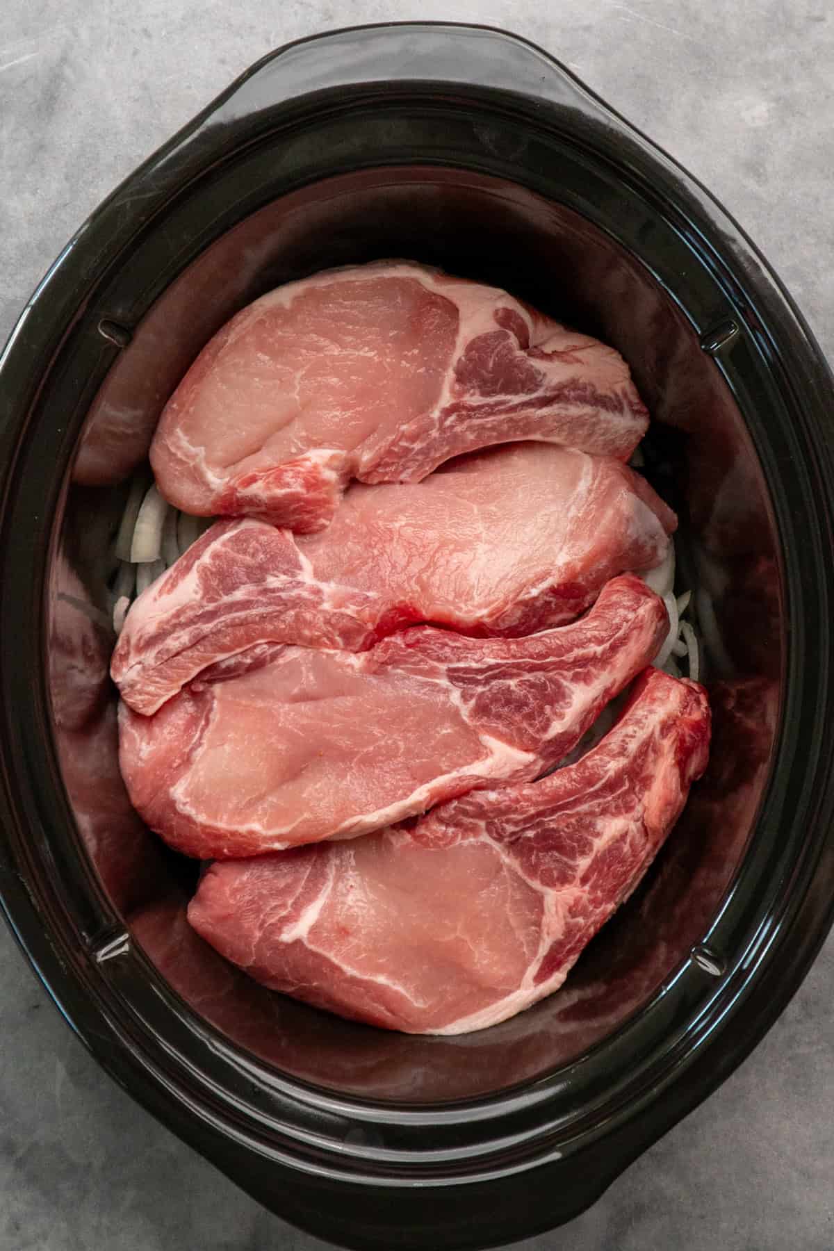 Pork chops on top of onions in a crock pot.