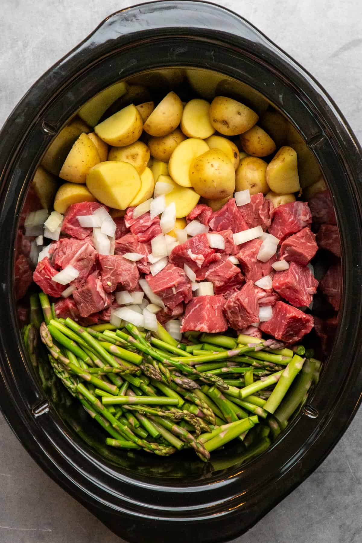 Steak, onions, potatoes, and asparagus in a crock pot.