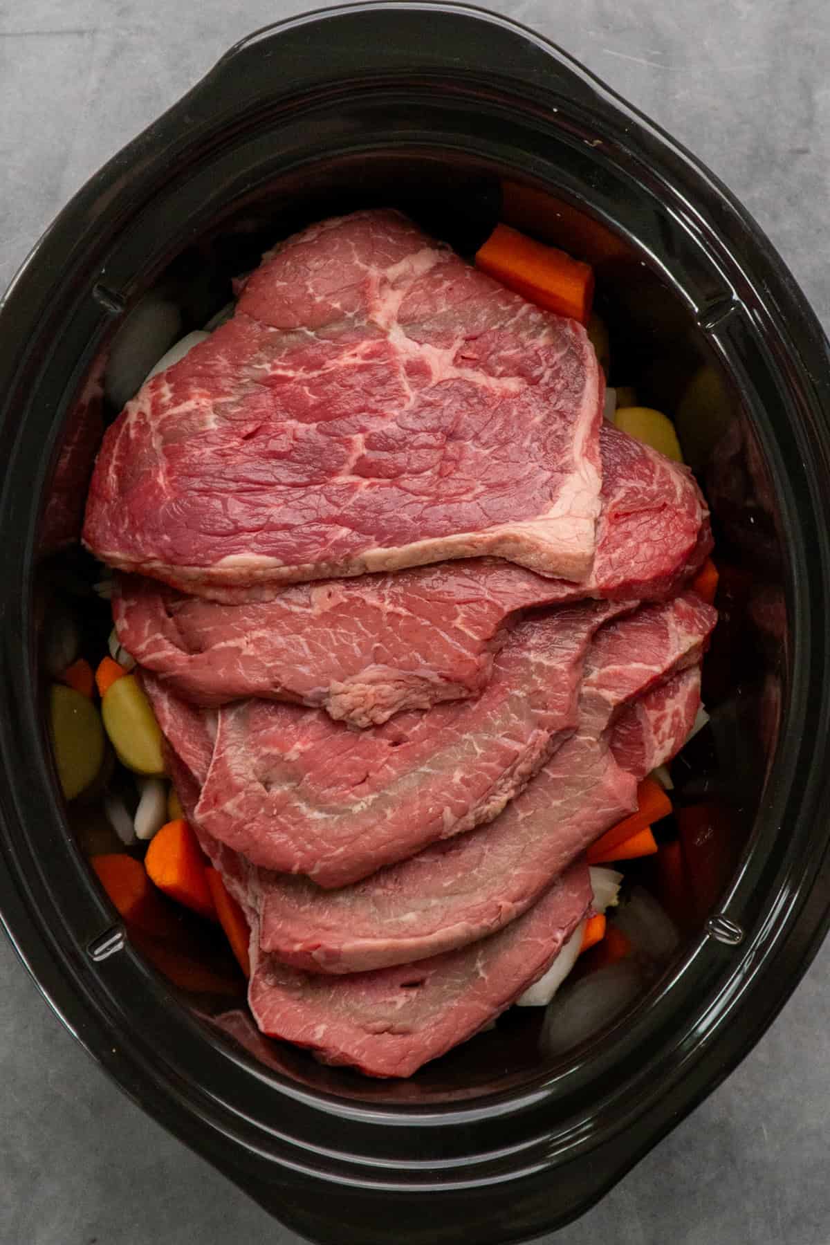 Steaks placed over the top of the vegetables in a slow cooker.