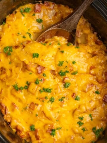 Crock Pot scalloped potatoes and ham with a wooden spoon ready to be served.