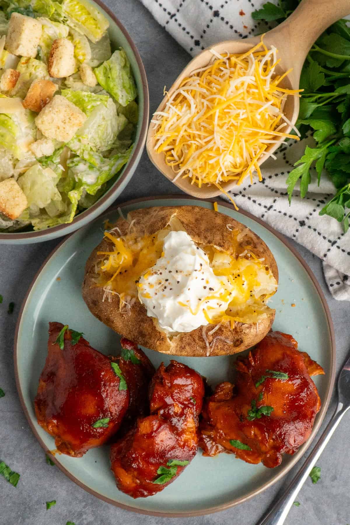 Slow cooker BBQ chicken thighs on a plate with a baked potato.