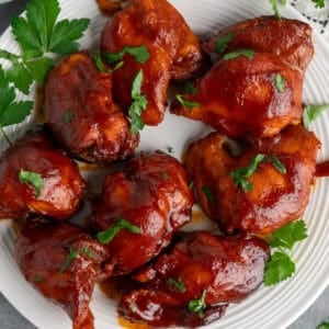 Slow cooker BBQ chicken thighs on a with plate with parsley in the background.