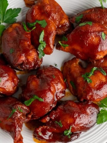 Slow cooker BBQ chicken thighs on a with plate with parsley in the background.