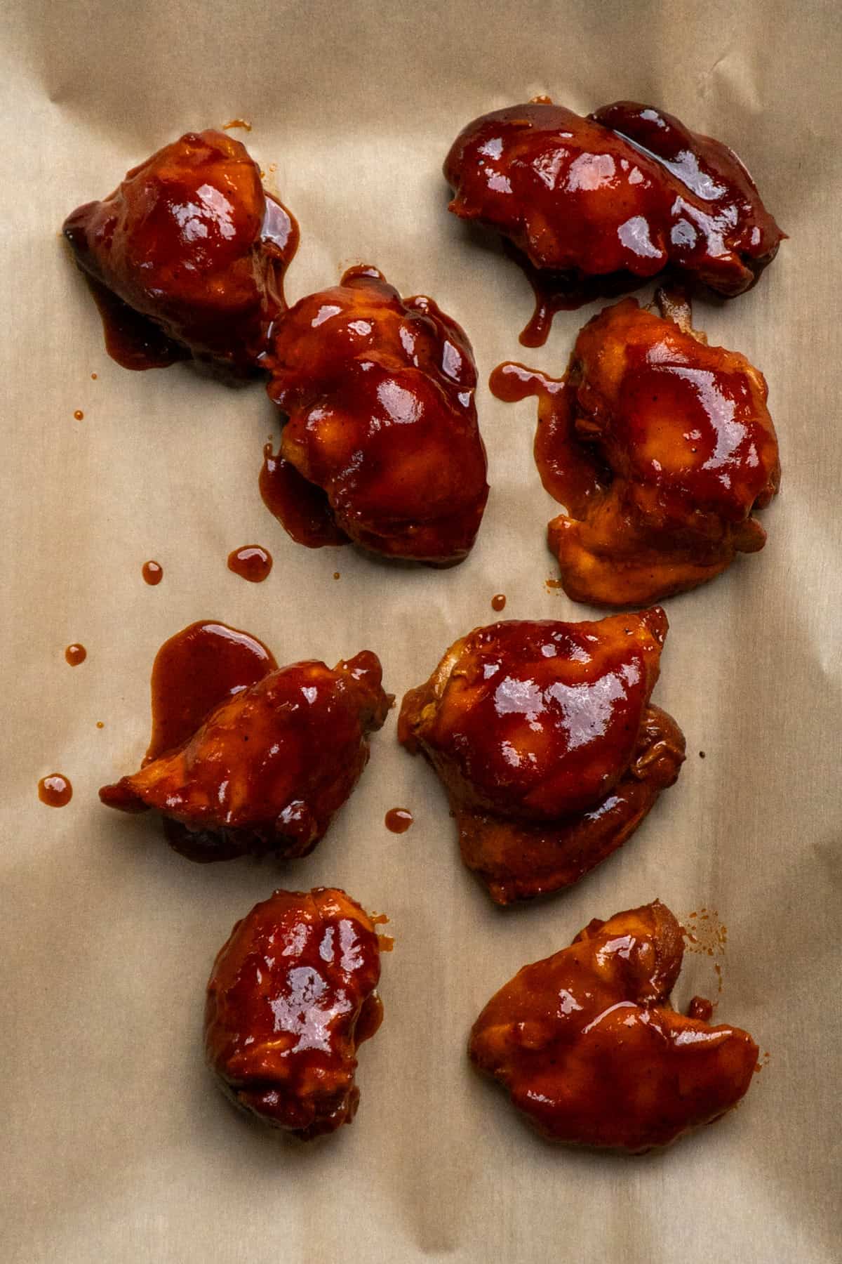 BBQ coated chicken thighs on a parchment lined baking sheet ready to be broiled.