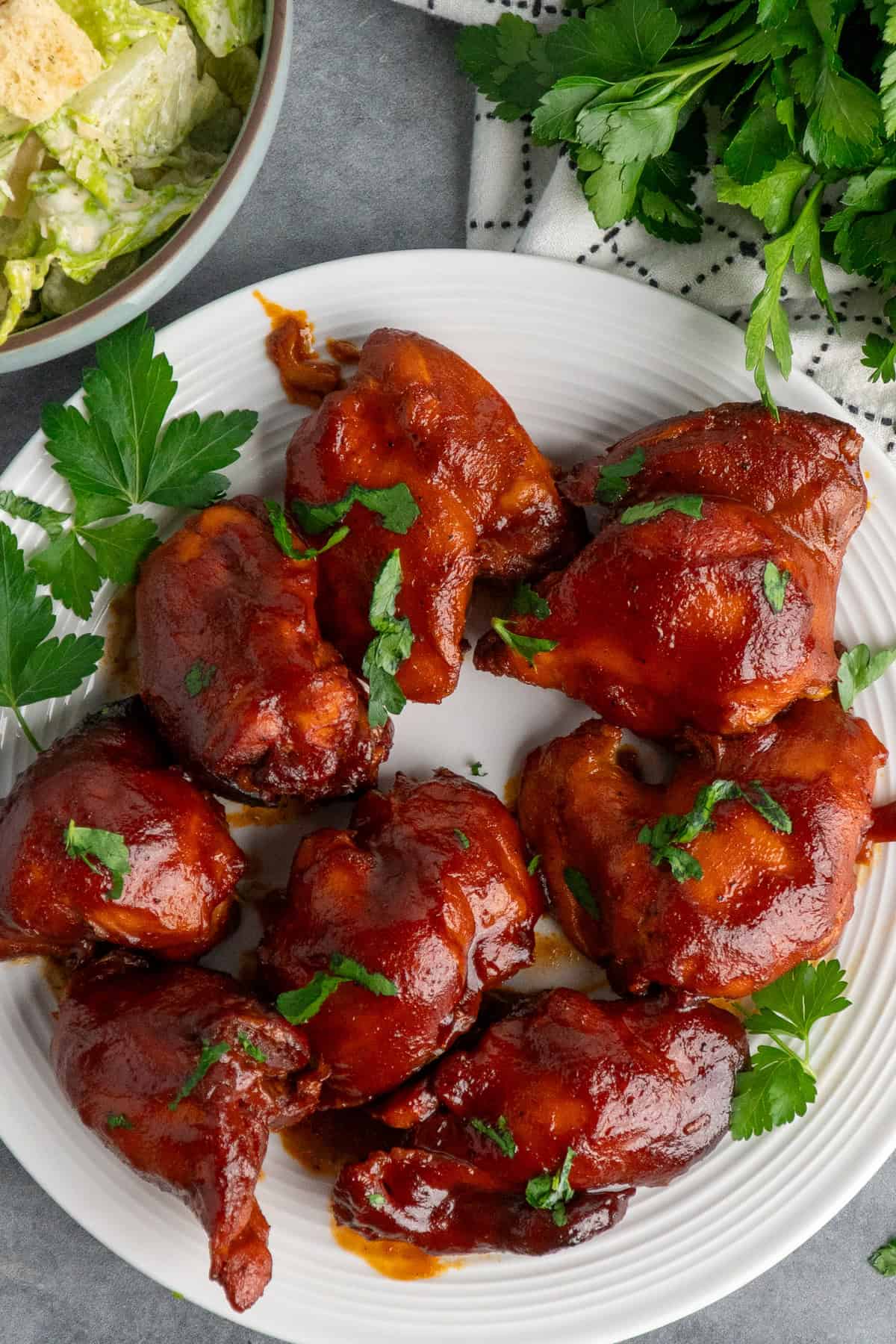 Slow cooker BBQ chicken thighs on a with plate with parsley in the background.