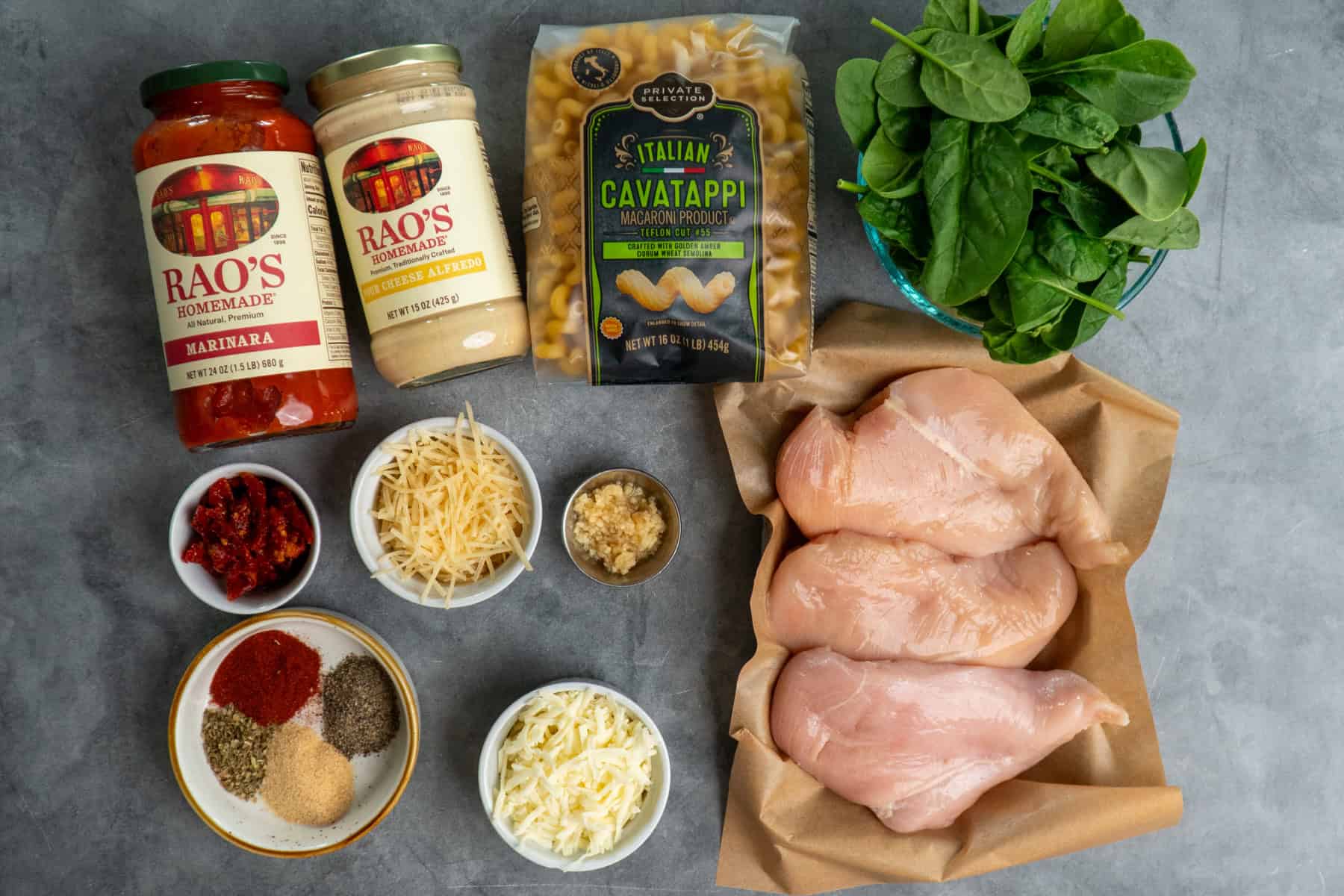 Ingredients to make marry me chicken pasta in bowls on a gray background.