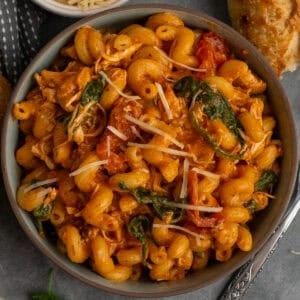 Crock pot marry me chicken pasta in a bowl with bread in the background.